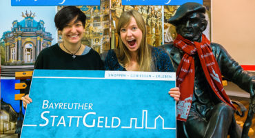 Zwei glückliche Frauen halten ein Plakat des Bayreuther Stattgeldes in die Luft