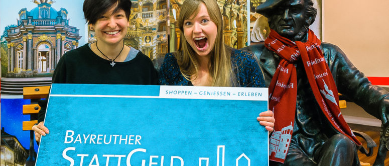 Zwei glückliche Frauen halten ein Plakat des Bayreuther Stattgeldes in die Luft