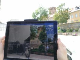Blick auf ein Tablet, das die geöffnete Future History-App zeigt, in der man an einem Ort zwischen historischen und aktuellen Bildaufnahmen hin und her wechseln kann