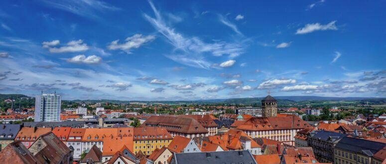 Der Blick auf das Dächermeer von Bayreuth von einem Kirchturm aus, der Himmel ist blau mit einigen Schleierwolken