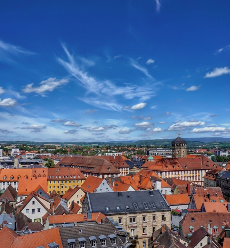Der Blick auf das Dächermeer von Bayreuth von einem Kirchturm aus, der Himmel ist blau mit einigen Schleierwolken