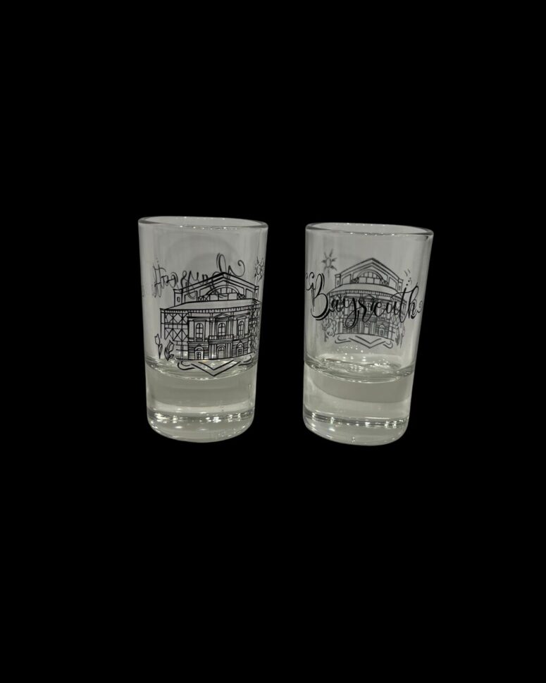 Zwei Klarglasbecher aus dem Bayreuth Shop zeigen schwarze Strichzeichnungen von Gebäuden und dekorative Schrift auf schwarzem Hintergrund.