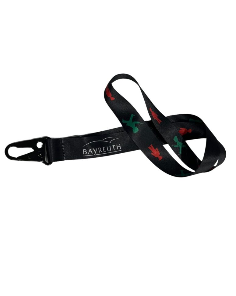Ein schwarzes Schlüsselband mit Metallverschluss, auf dem das Wort BAYREUTH in weißer Schrift und ein stilisiertes Liniendesign zu sehen ist. Erhältlich im Bayreuth Shop, zeigt es außerdem rote und grüne Symbole, die an Ampelmännchen erinnern.