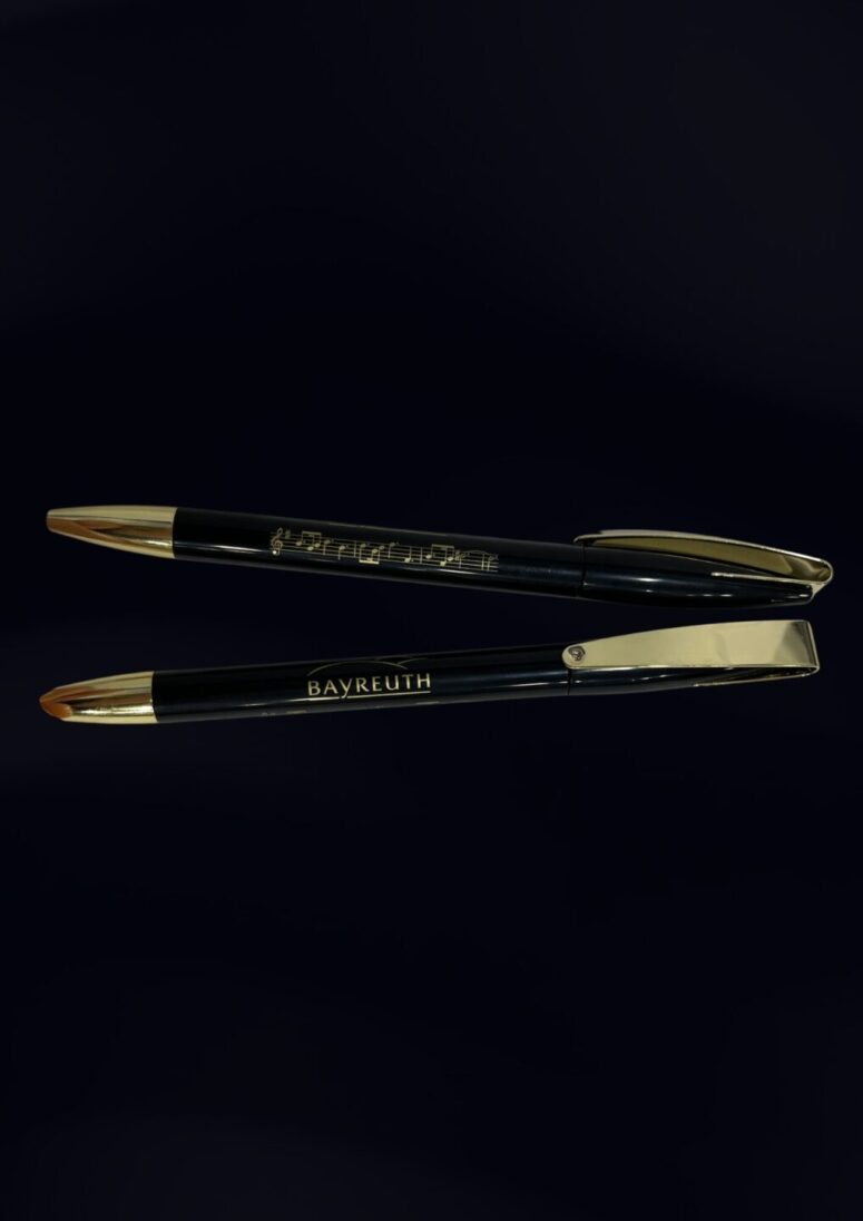 Zwei schwarze Stifte mit goldfarbenen Spitzen und Clips sind parallel auf einem dunklen Hintergrund platziert. Auf dem einen Stift steht BAYREUTH, was an die Eleganz eines Artikels aus dem Bayreuth Shop erinnert, während der andere Stift eine goldene Schrift in einer anderen Schriftart aufweist.
