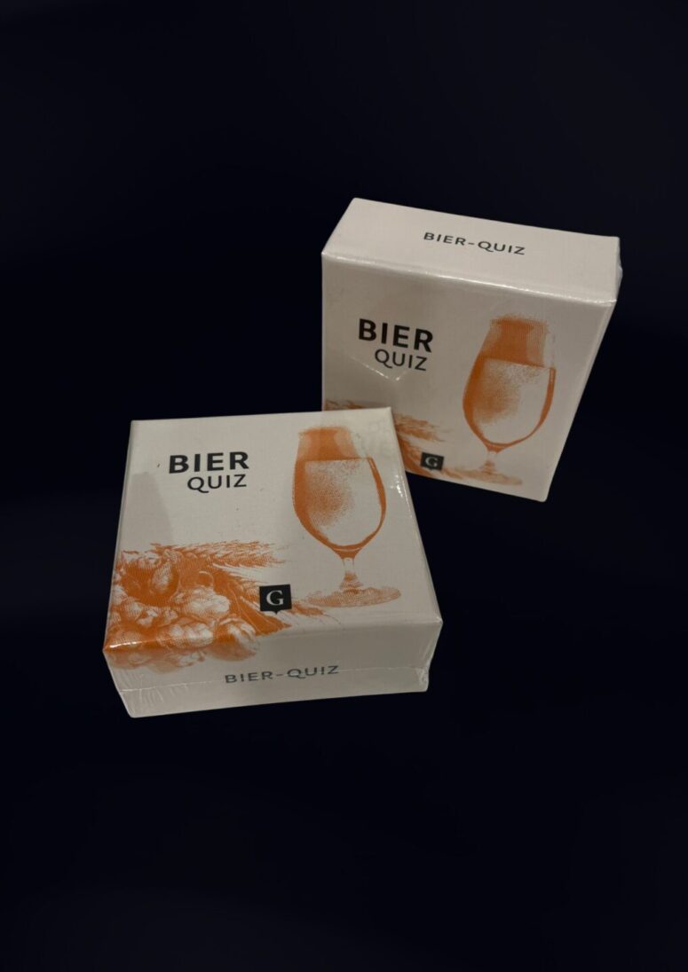 Zwei weiße Schachteln mit der Aufschrift "Bier Quiz", die ein Bierglas und eine Hopfenillustration zeigen, sind versiegelt und stehen schräg vor einem dunklen Hintergrund. Sie sind perfekt für Fans und eine einzigartige Ergänzung für jede Bayreuth-Shop-Sammlung.
