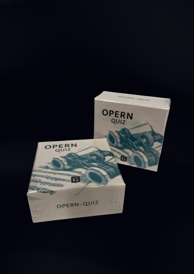 Zwei Schachteln mit der Aufschrift OPERN-QUIZ, auf deren Verpackung Operngläser und Noten abgebildet sind, stehen vor einem dunklen Hintergrund - ein exklusives Fundstück aus dem Bayreuth-Shop.