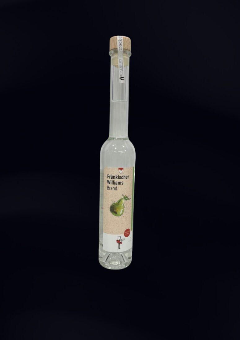 Eine hohe, klare Glasflasche mit einem Holzdeckel, die Fränkischer Williams Brand, einen deutschen Birnenbrand, enthält. Auf dem Etikett sind eine grüne Birne und ein deutscher Text auf weißem Hintergrund abgebildet, erhältlich im Bayreuth Shop.
