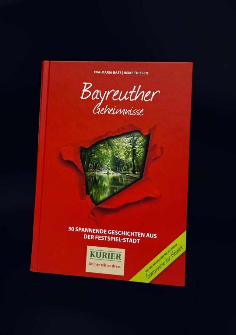 Ein rotes Buch mit dem Titel Bayreuther Geheimnisse mit einem zerrissenen Papiermotiv, das eine malerische Park- und Wasseransicht zeigt, ziert den Einband. Entdecken Sie 50 spannende Geschichten aus der Festspiel-Stadt - ab sofort im Bayreuth Shop erhältlich.
