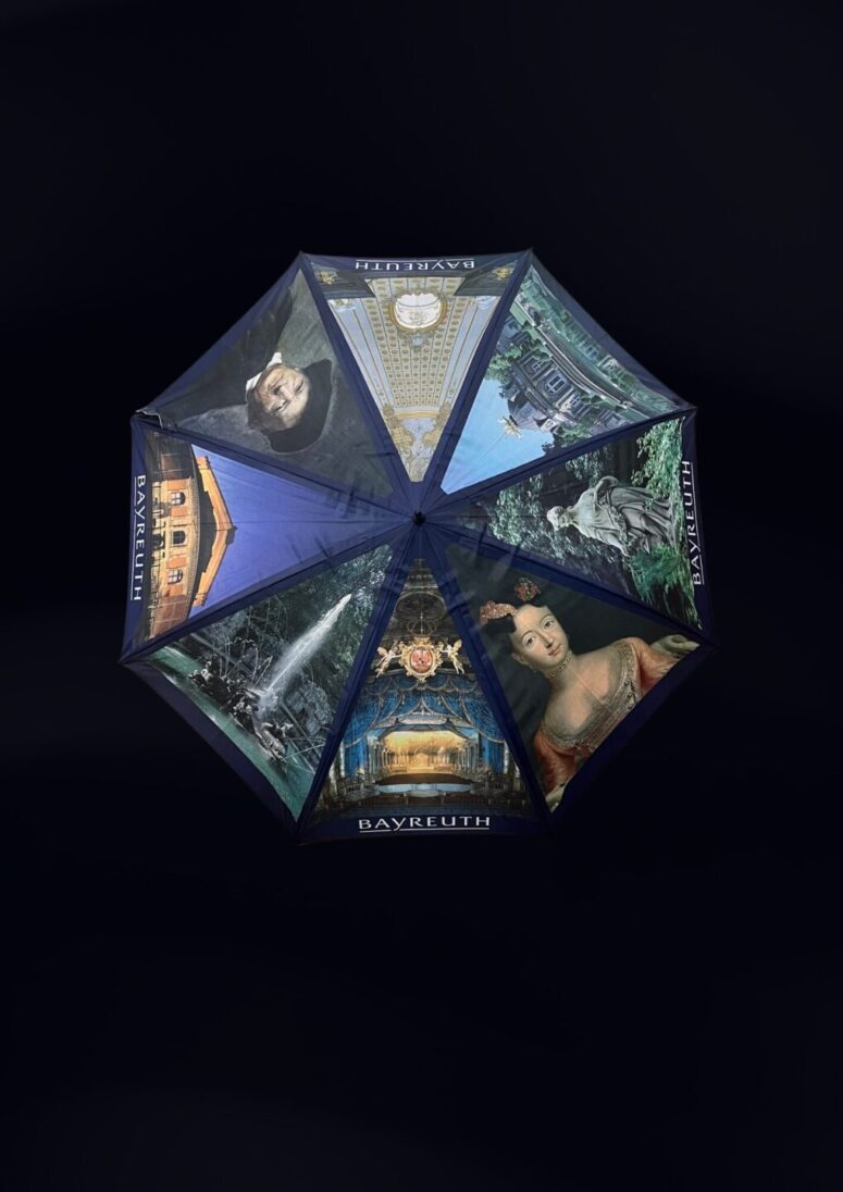 Ein farbenfroher Regenschirm, der von oben betrachtet wird und auf dem Porträts, historische Gebäude, Statuen und Wahrzeichen - alle mit der Aufschrift Bayreuth - vor einem dunklen Hintergrund zu sehen sind. Entdecken Sie dieses einzigartige Design im Bayreuth Shop.