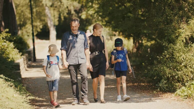 Eine vierköpfige Familie, zwei Erwachsene und zwei Kinder, geht an einem sonnigen Tag gemeinsam auf einem von Bäumen gesäumten Weg in einem Park spazieren. Dieser entspannte und glückliche Moment ist in diesem CC0-Bilder Bild perfekt eingefangen.