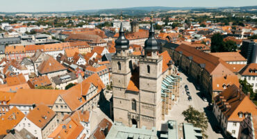 Luftaufnahme einer europäischen Stadt mit roten Ziegeldächern, engen Straßen und einer markanten zweitürmigen Kirche im Zentrum, umgeben von historischen Gebäuden und sanften Hügeln - perfekt für alle, die CC0-Bilder für kreative Projekte suchen.
