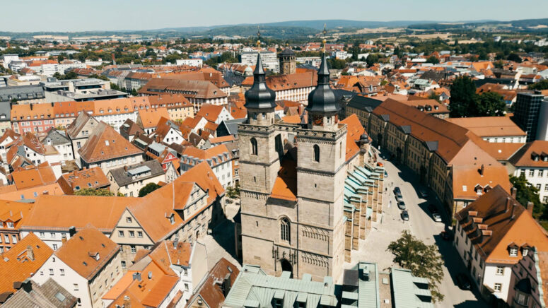 Luftaufnahme einer europäischen Stadt mit roten Ziegeldächern, engen Straßen und einer markanten zweitürmigen Kirche im Zentrum, umgeben von historischen Gebäuden und sanften Hügeln - perfekt für alle, die CC0-Bilder für kreative Projekte suchen.