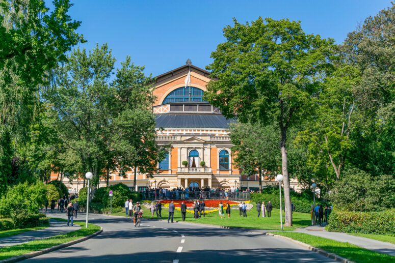 Menschen laufen und versammeln sich vor einem großen, historischen Gebäude mit Bogenfenstern und dekorativer Architektur, umgeben von üppigen grünen Bäumen und einem gepflegten Rasen, unter einem strahlend blauen Himmel - perfekt für CC0-Bilder-Sammlungen.