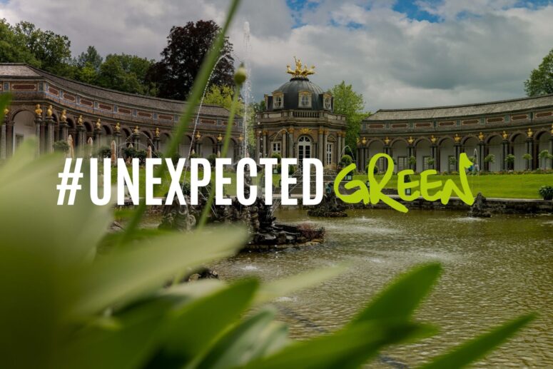 Ein Palast im Barockstil, der an Bayreuth erinnert, mit einem Springbrunnen und üppigem Grün. Über dem Bild ist in großer Schrift der Schriftzug #UNEXPECTED GREEN zu lesen. Im Vordergrund sind farbenprächtige Pflanzen zu sehen, während der Hintergrund einen bewölkten Himmel und exquisite architektonische Details zeigt.