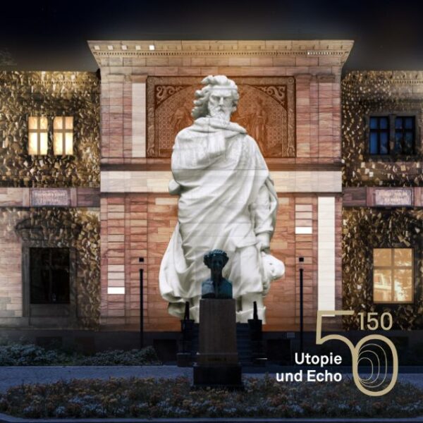 Nachts wird eine große weiße Statue auf eine Gebäudefassade projiziert, vor der eine kleinere Statue steht. In der rechten unteren Ecke erscheint der Text „150 Utopie und Echo“.