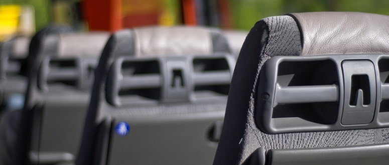 Nahaufnahme der Rückseiten mehrerer grauer und schwarzer Sitze im Inneren eines Busses, die die Atmosphäre einer typischen Busreise einfängt, mit verschwommenen Fenstern und vorbeiziehender Landschaft im Hintergrund.
