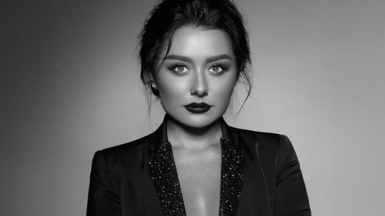 Schwarz-Weiß-Porträt einer Frau mit dunklem Haar, auffälligem Lippenstift und ausdrucksstarken Augen, die einen Blazer mit funkelndem Revers trägt und vor einem schlichten Hintergrund direkt in die Kamera blickt – ein Bild, das an die zeitlose Eleganz der renommierten Galerien im Friedrichsforum erinnert.