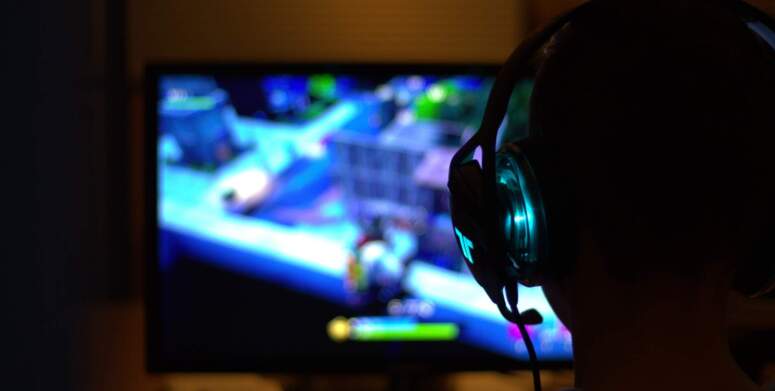 Eine Person, die leuchtende Gaming-Kopfhörer trägt, spielt ein Videospiel auf einem Monitor.