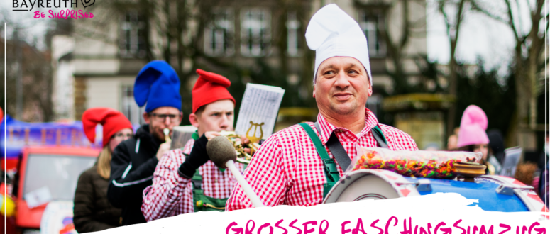 Ein Mann mit Kochmütze und rotem Karohemd spielt während eines Faschingsumzugs auf einer Trommel; dazu steht der Text Großer Faschingsumzug, Sonntag, 7. Februar 2027.