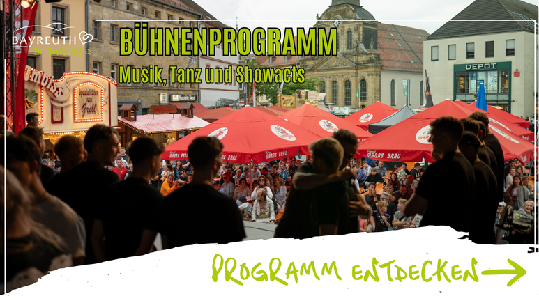 Eine Menschenmenge verfolgt eine Fasching-Aufführung auf einer Freilichtbühne unter roten Sonnenschirmen auf einem Stadtplatz, über der die Aufschriften BÜHNENPROGRAMM und PROGRAMM ENTDECKEN zu lesen sind.