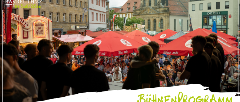 Eine Menschenmenge aus Mitgliedern lokaler Vereine verfolgt auf einer Freiluftbühne bei einem Fest in Bayreuth eine Darbietung im Rahmen eines Faschingsumzugs, umgeben von roten Biermarkisen und Marktständen.