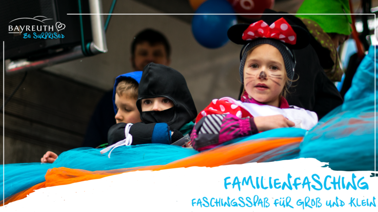 Kinder in Kostümen fahren auf einem Festwagen beim Faschingsumzug mit, auf dem der Schriftzug FAMILIENFASCHING – FASCHINGSSPASS FÜR GROSS UND KLEIN zu sehen ist.